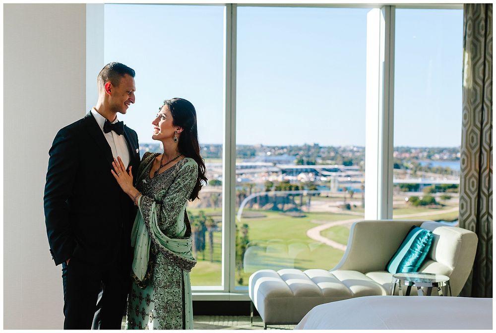 Elegant couple in formal attire share an intimate moment by large windows overlooking a scenic view.