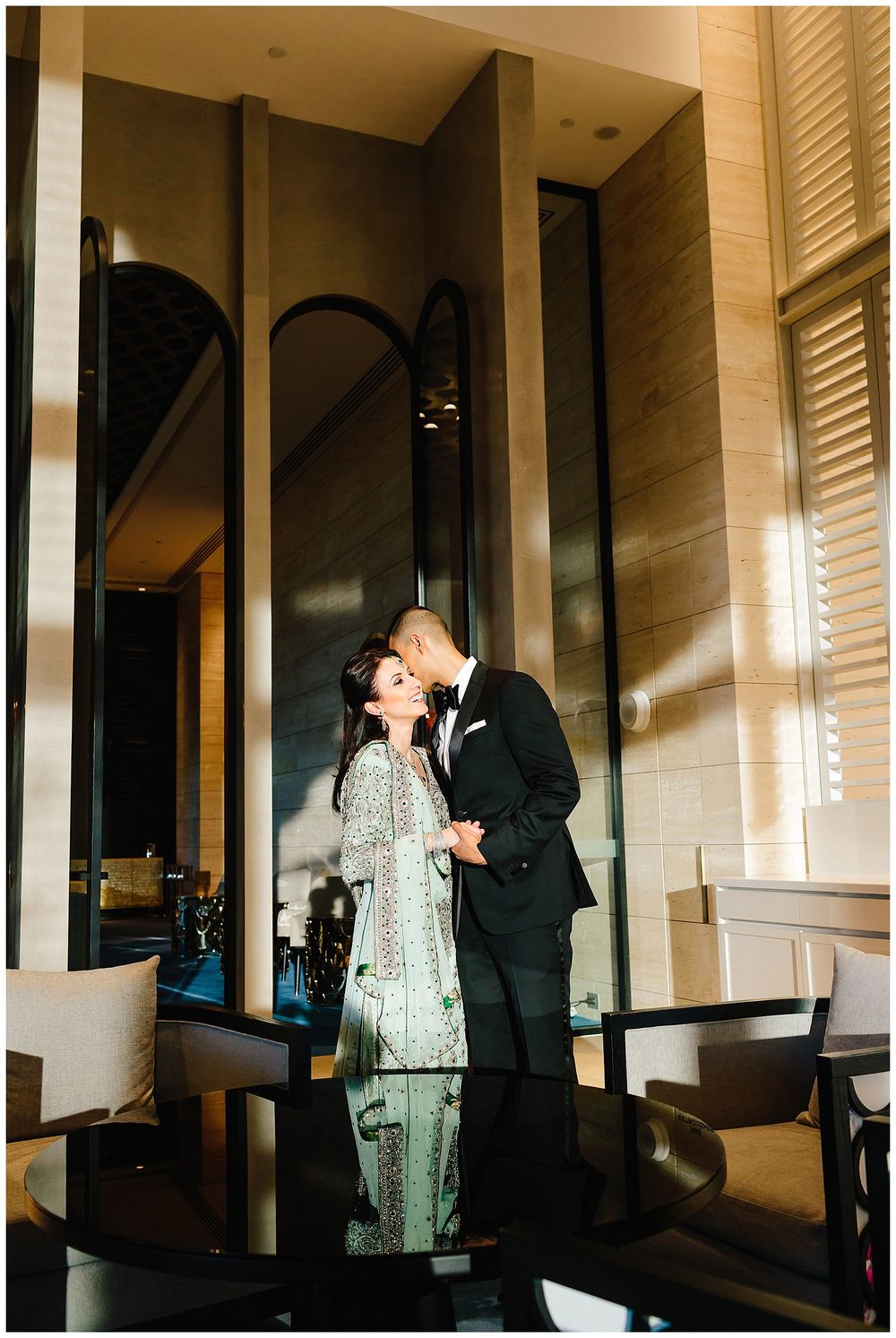 A couple shares an intimate moment in an elegant hotel lobby with reflective mirrors and warm lighting.