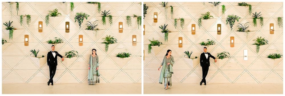 A couple walks together against a decorative wall with hanging plants and modern lighting.