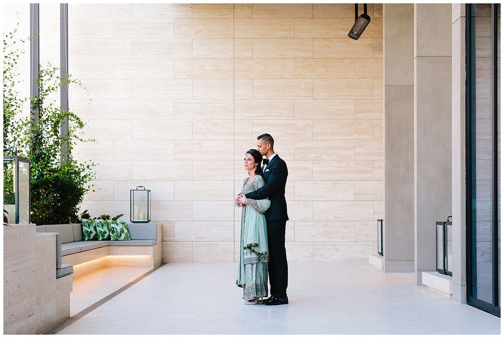 A tender moment between a couple in formal wear near modern architecture and greenery.