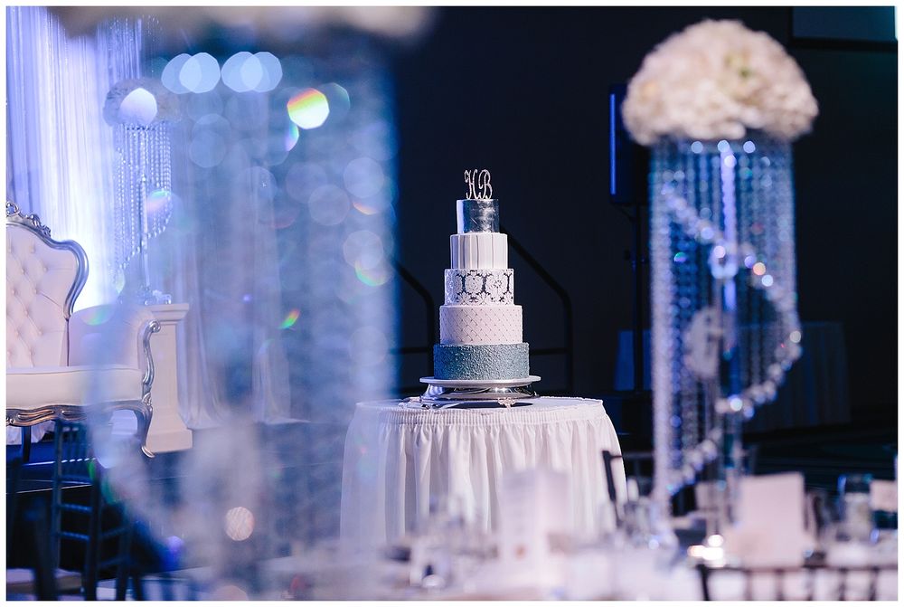 Elegant white tiered wedding cake displayed on round table with dramatic blue lighting.