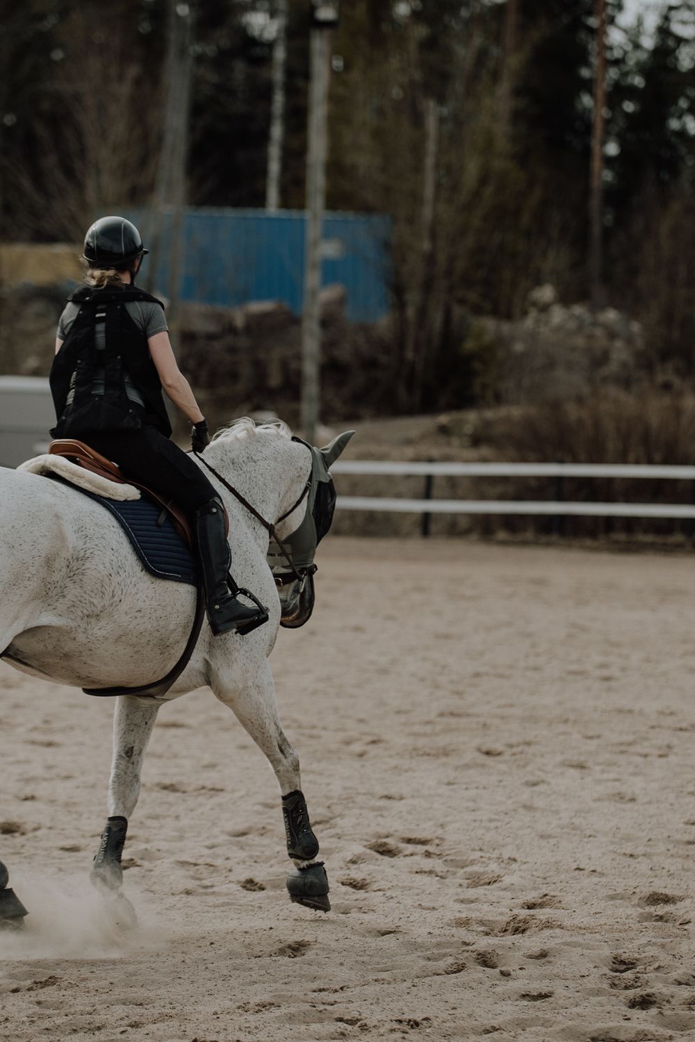 Rider on white horse galloping through sandy arena during training.