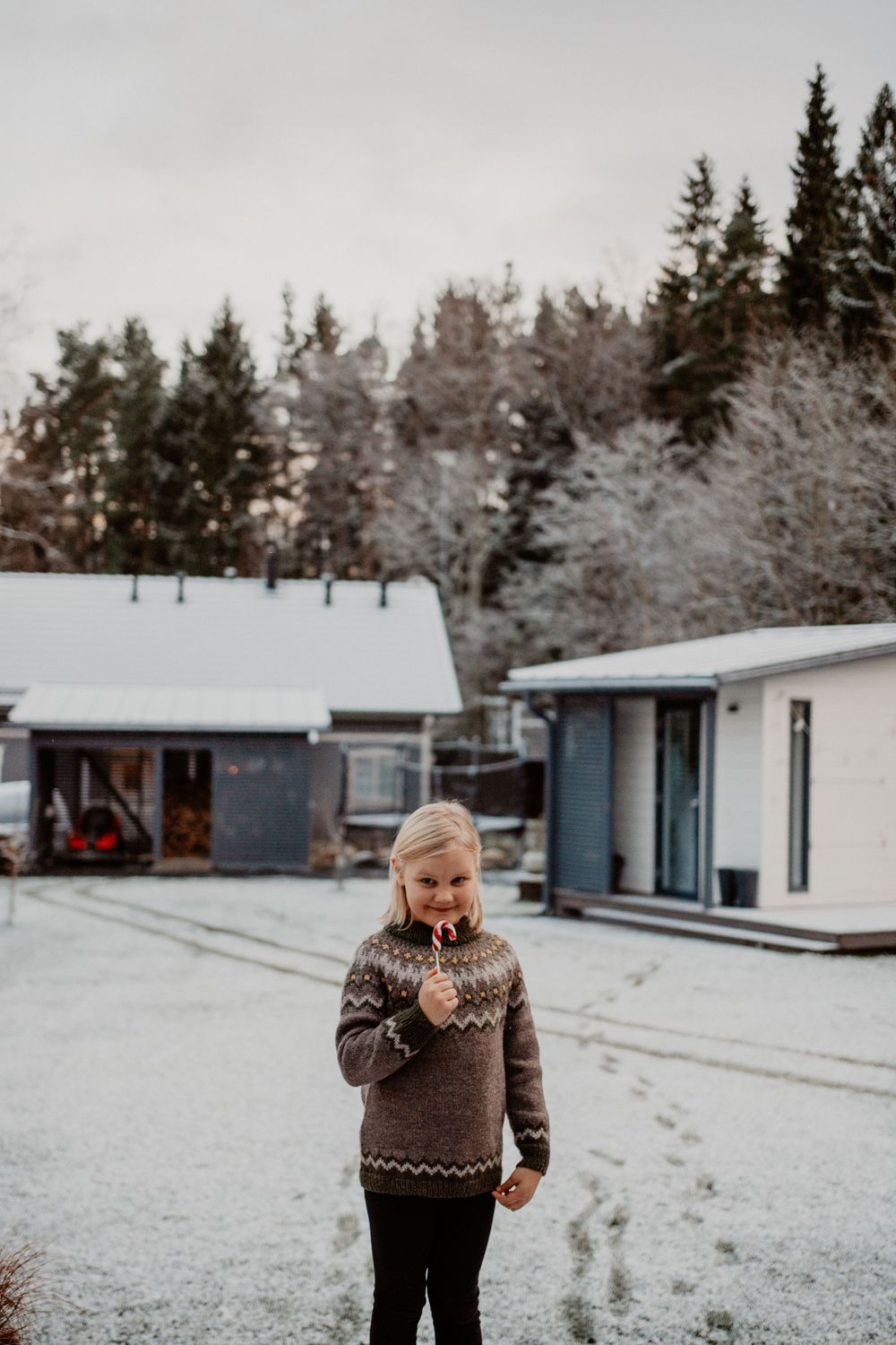 Person in a brown sweater standing in a snowy landscape with cabins in the background.