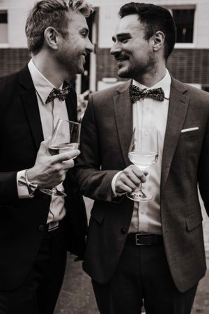Das Ehepaar in Anzug und fliege prostet sich zu. LGBTQ+ Hochzeit
