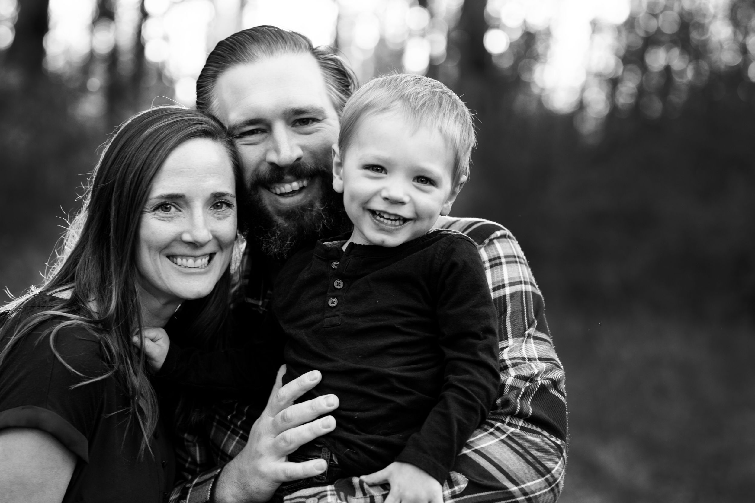 Mom dad and kid smile naturally and snuggle in the park