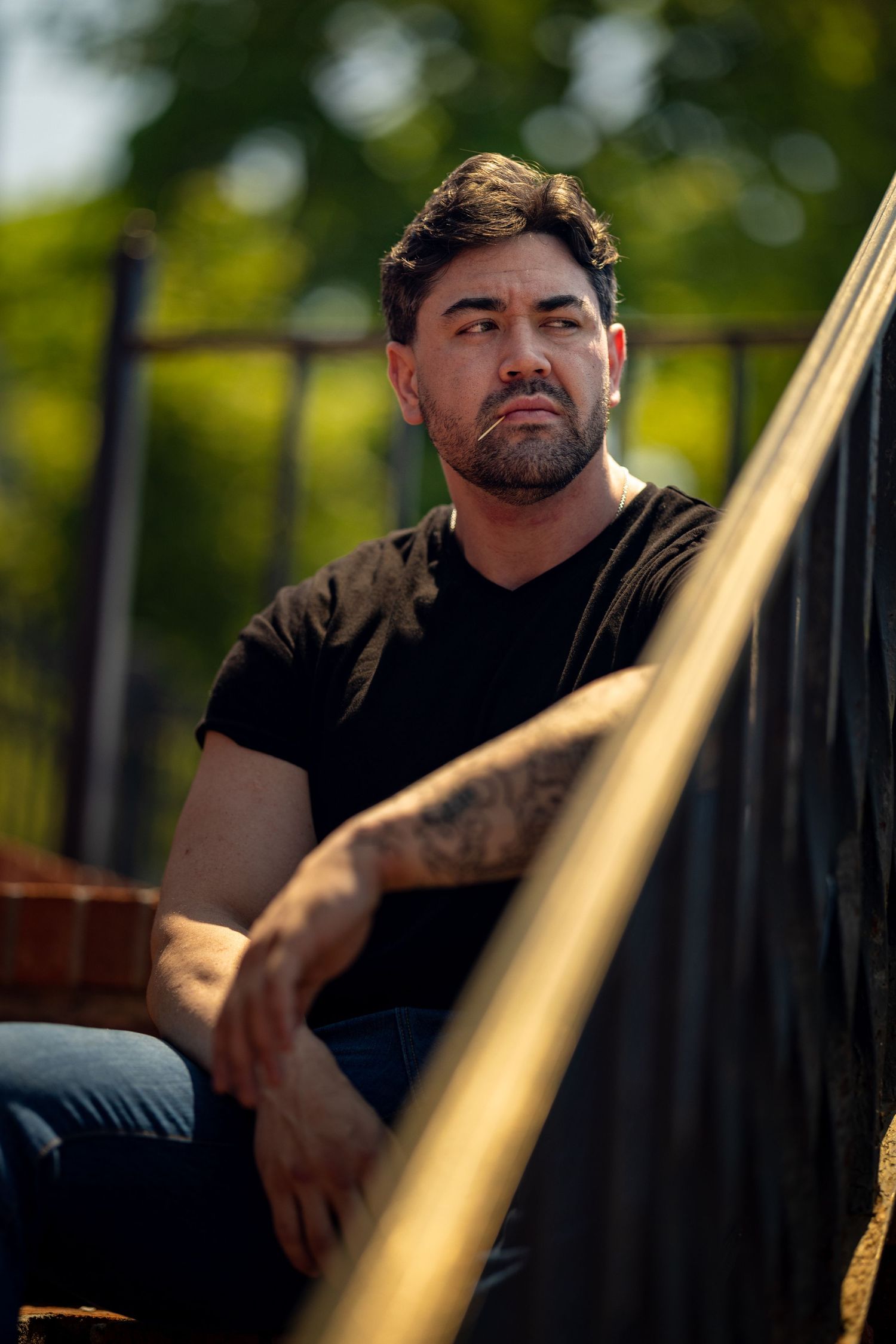 Man in black t-shirt sitting outdoors with golden lighting and bokeh effect.