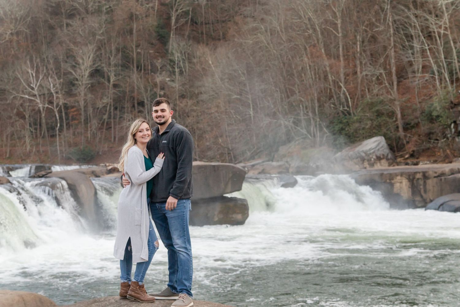 A couple embraces in front of a dramatic waterfall on a misty day.