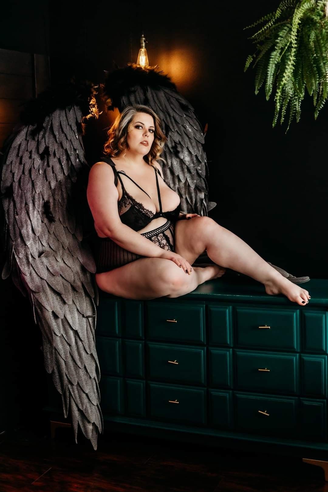 Dramatic portrait with large decorative angel wings against dark green dresser.