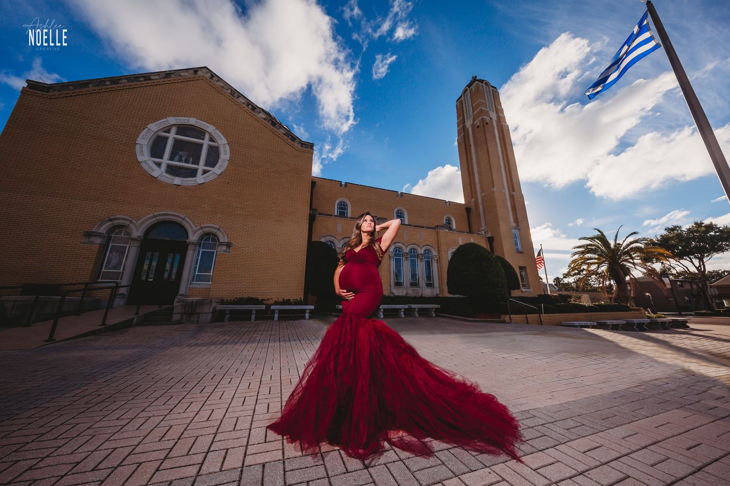 Dramatic maternity photo in red flowing gown in front of church with Greek flag.