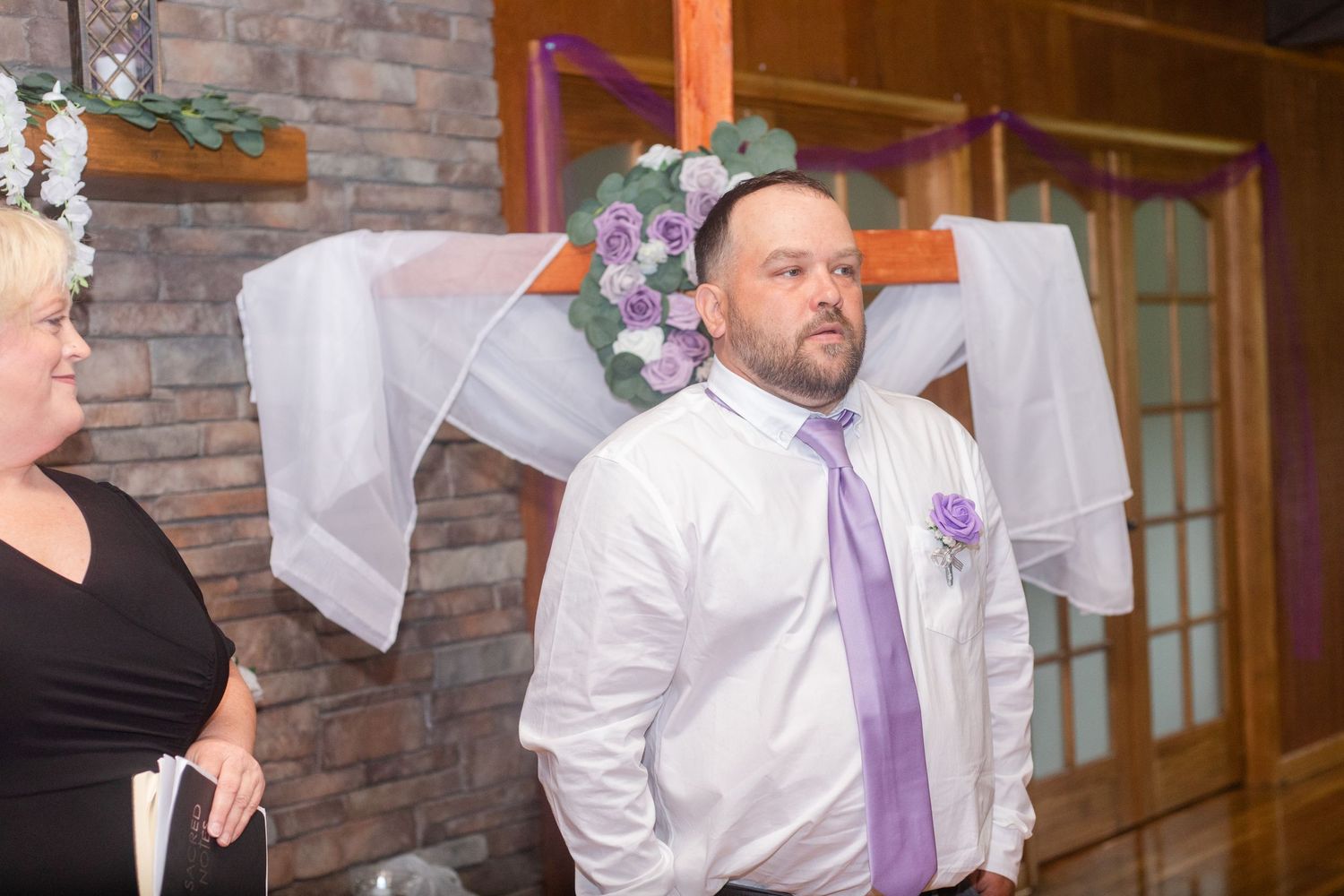 Wedding party members in white shirts and purple ties gather in a rustic venue.