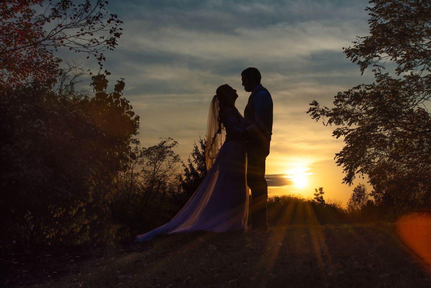 Sunset silhouettes of couple on hill with dramatic orange sky and trees.