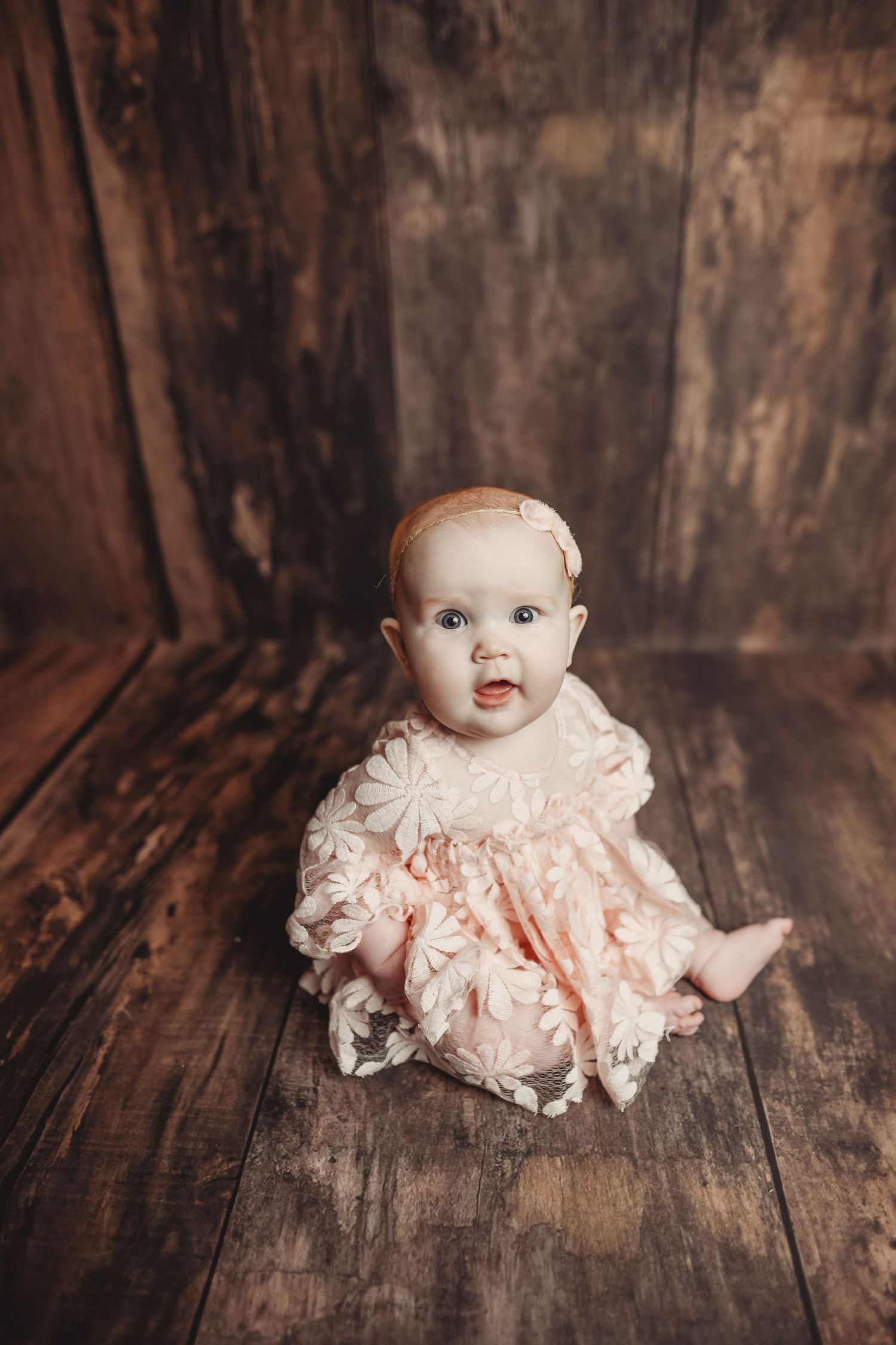 Delicate peach lace dress photographed on rustic wooden floor with dark backdrop.