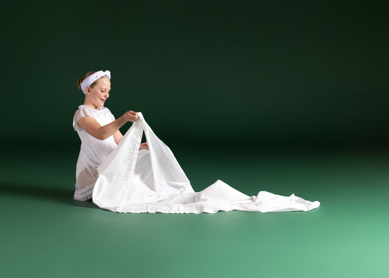 Small child in white sailor outfit sitting with flowing fabric in studio setting.