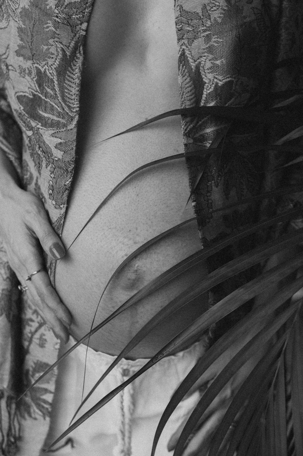 Artistic black and white maternity photo with palm leaves creating shadows.