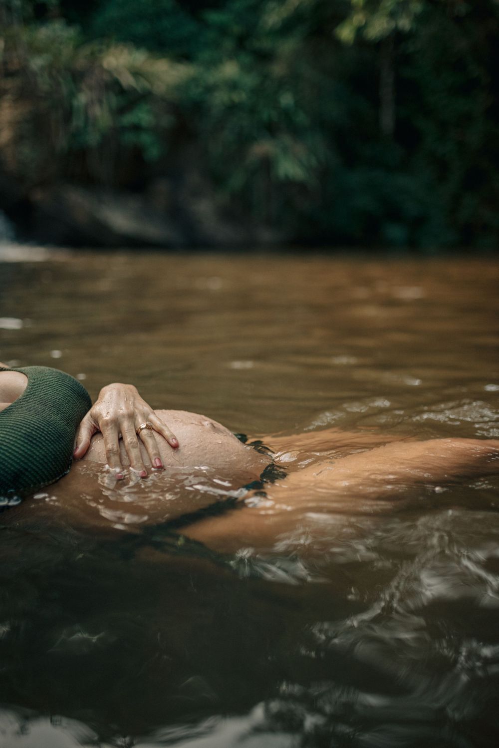 Artistic maternity photo with water immersion in natural stream setting.