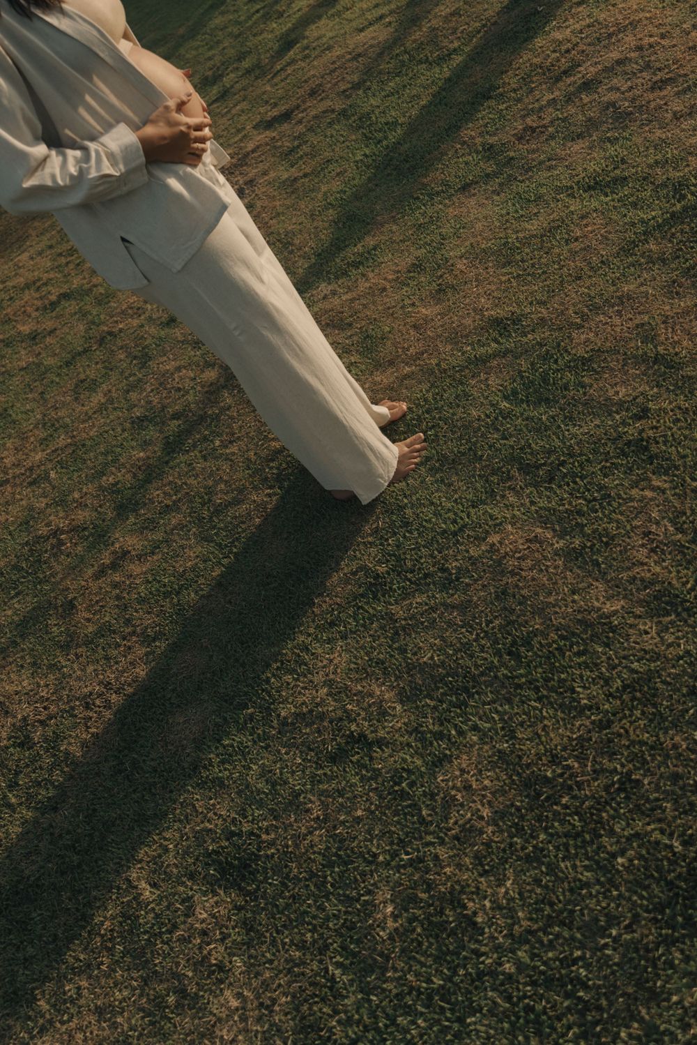 Cropped view of a person in white clothing standing on grass with a long shadow.