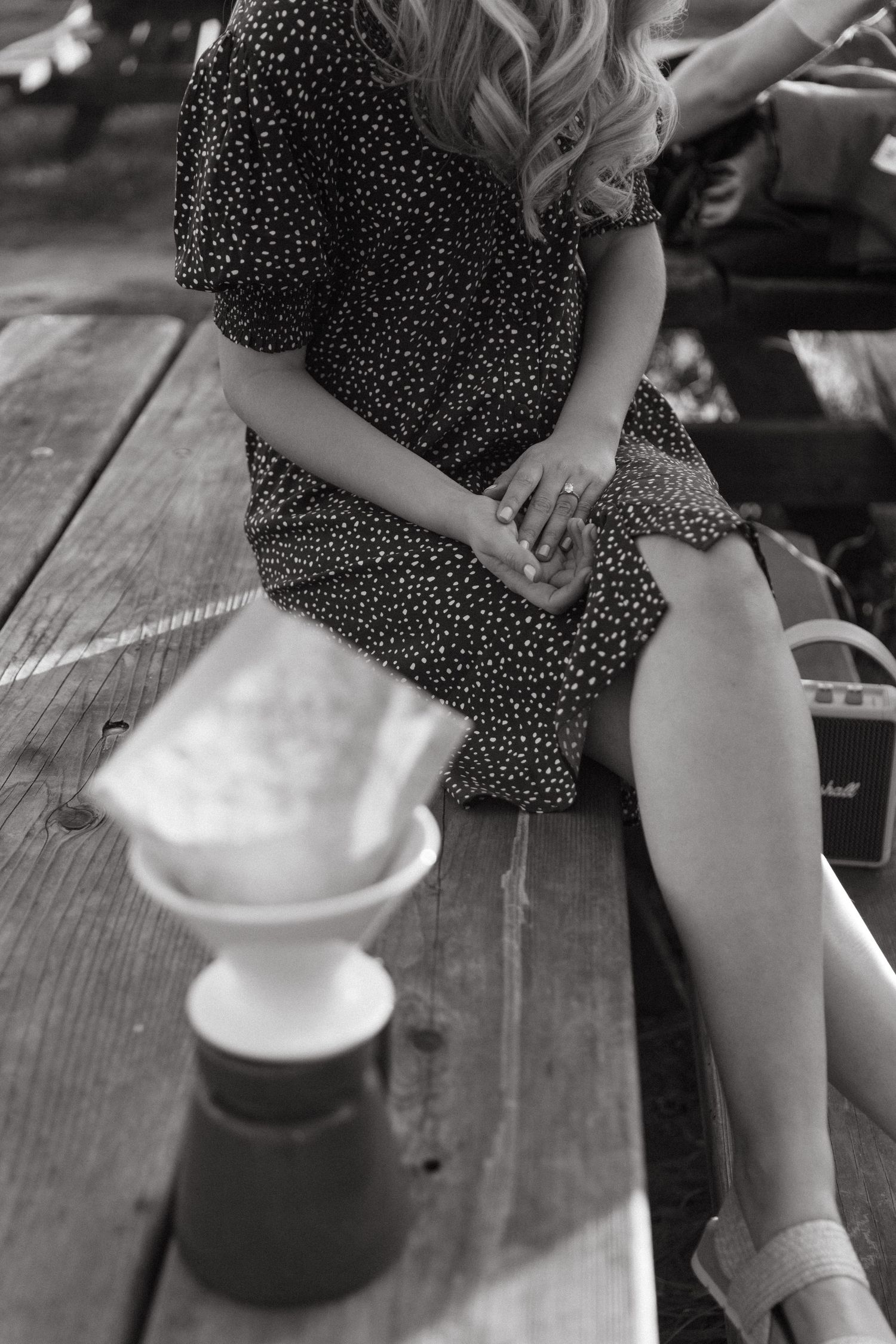 A woman in a polka dot dress sits on wooden decking beside a coffee maker.