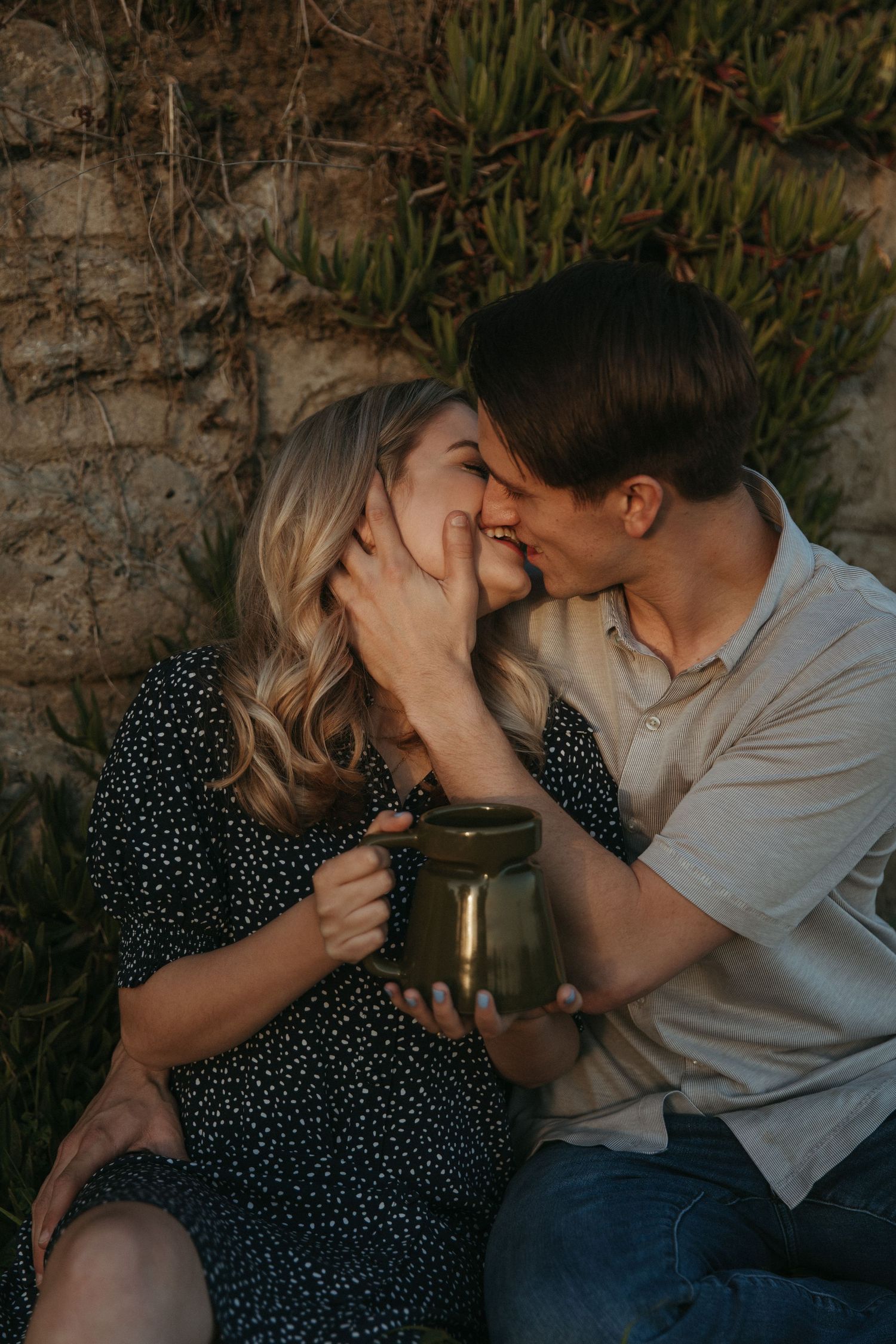 An intimate moment shared between a couple with a coffee mug against a stone wall.