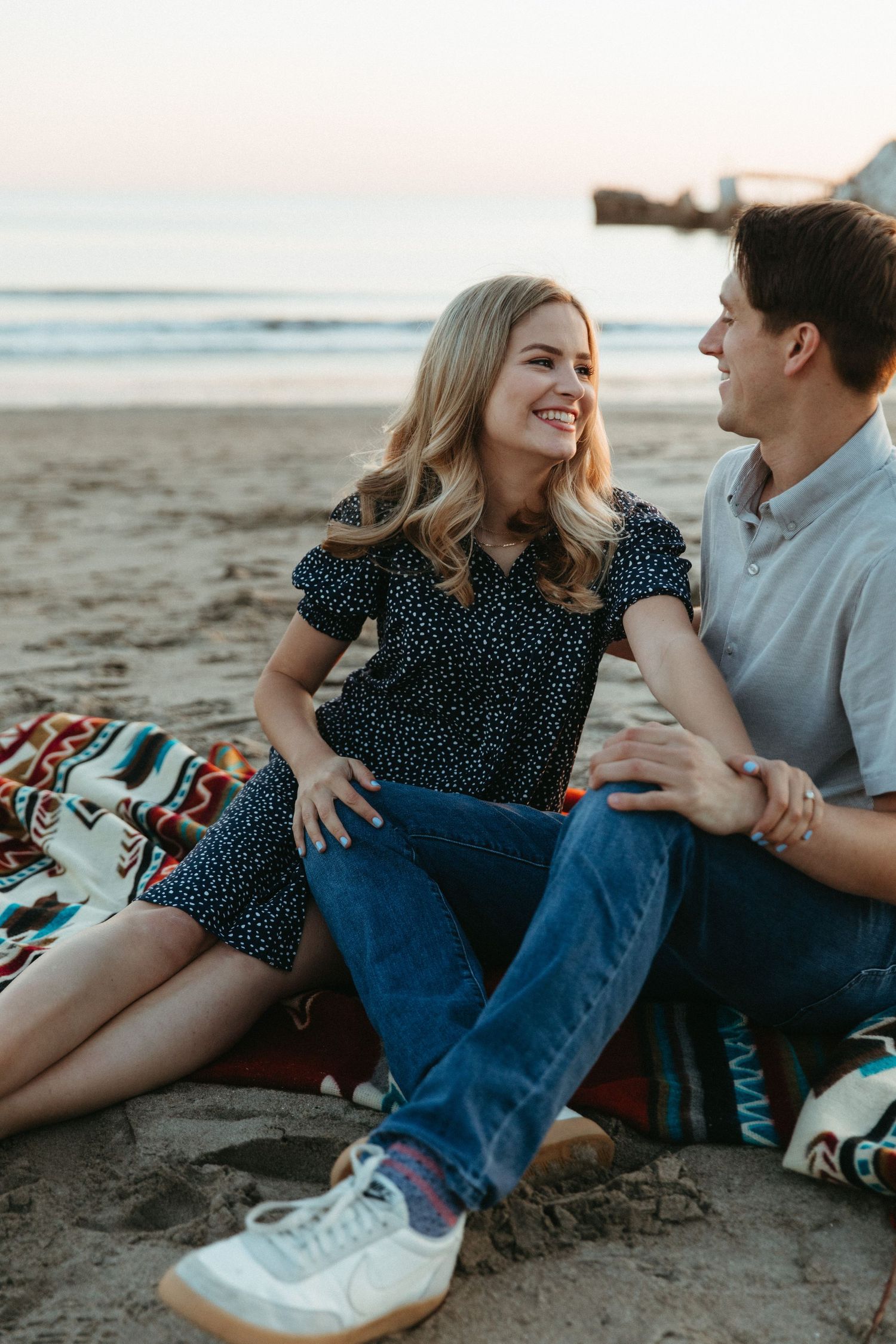 Couple sitting on a blanket at the beach during golden hour sharing a joyful moment together.