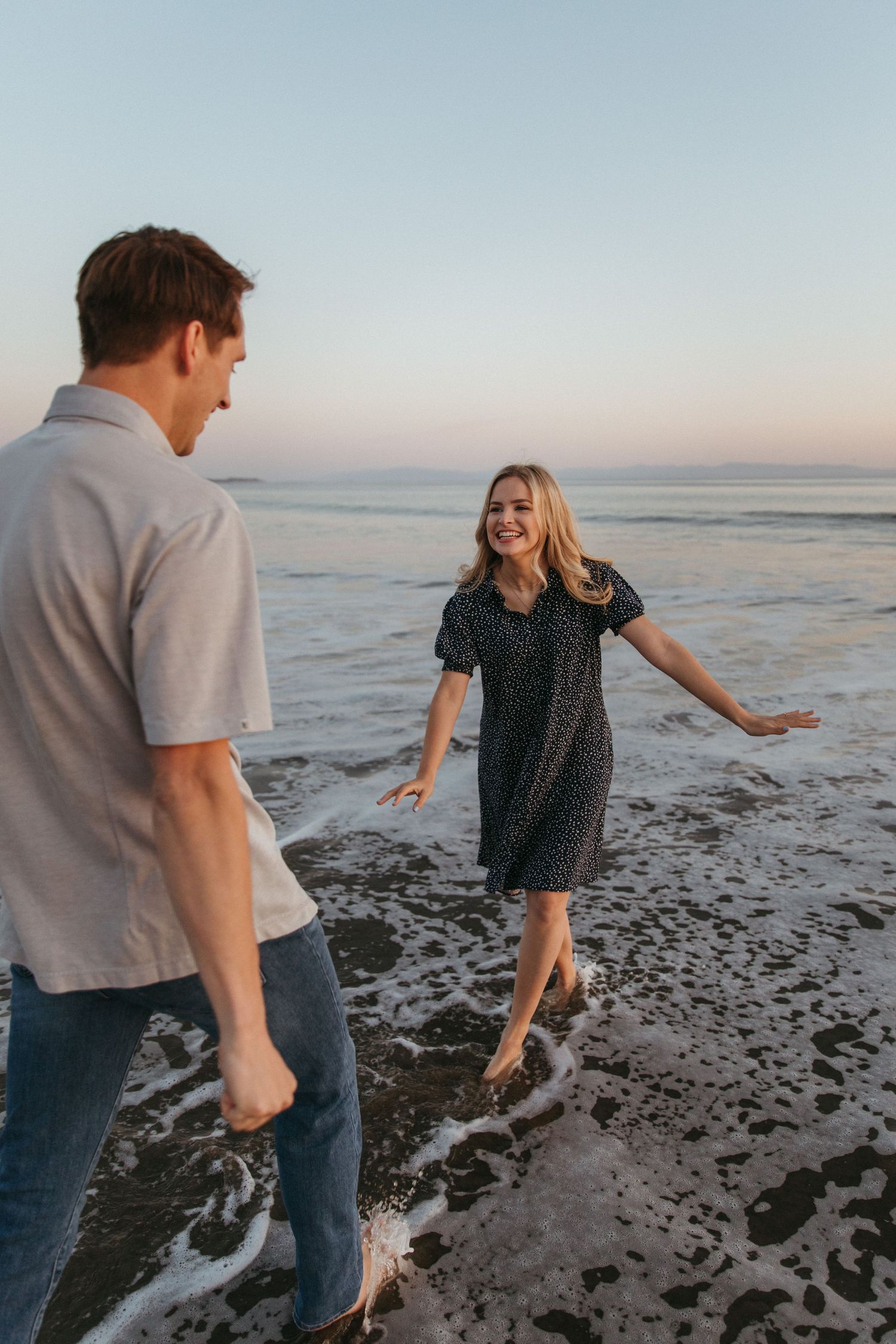 Playful couple enjoying a carefree moment at the beach with waves crashing at their feet.