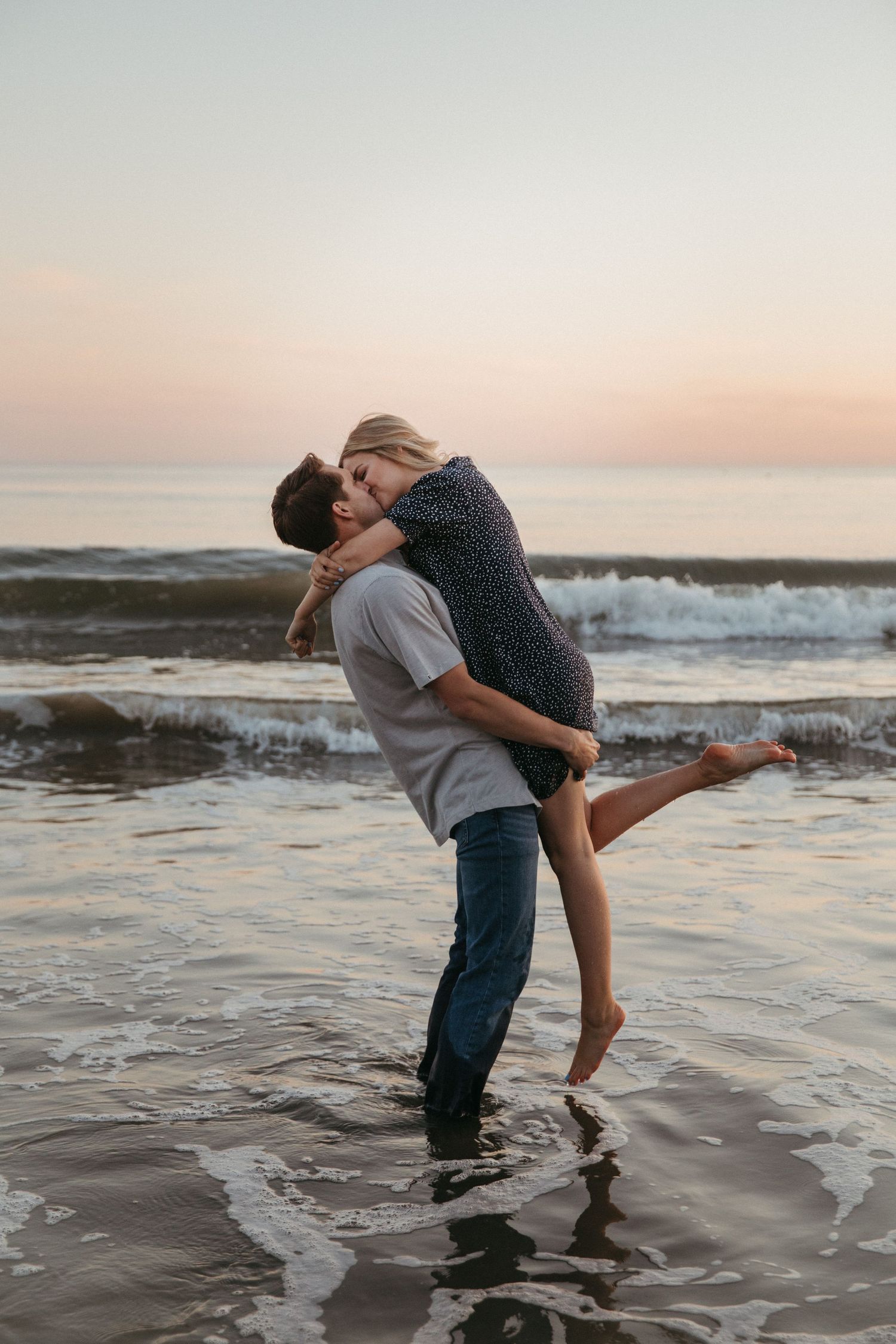Romantic beach moment with waves crashing as couple embraces during sunset photoshoot.