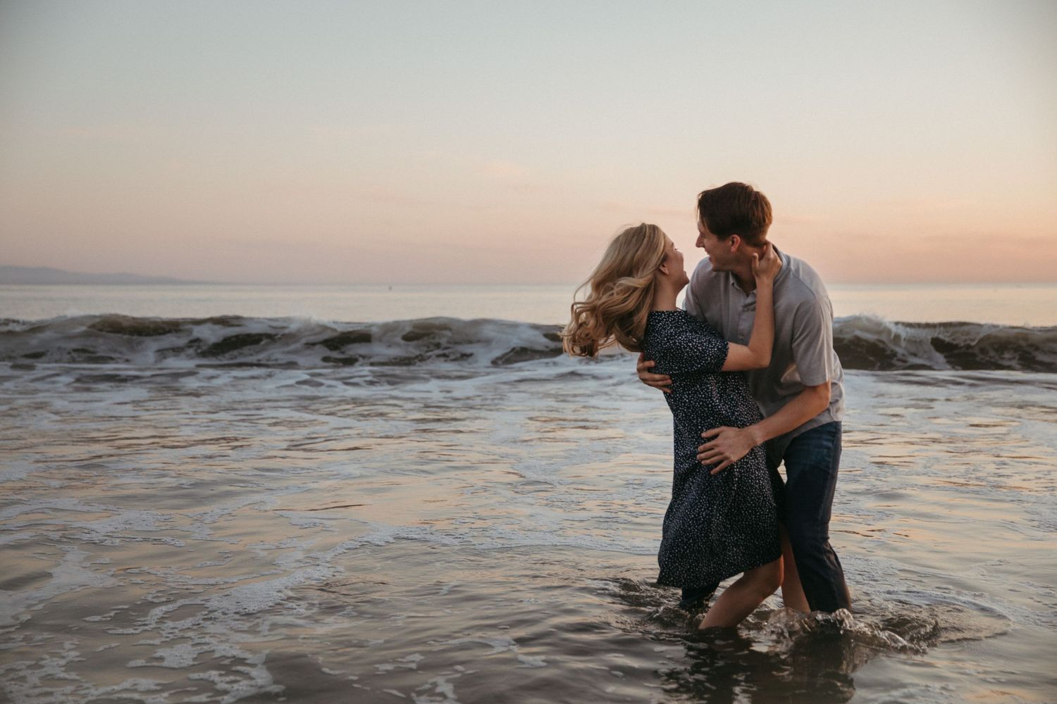 A couple shares an intimate moment while standing in shallow ocean water at sunset.