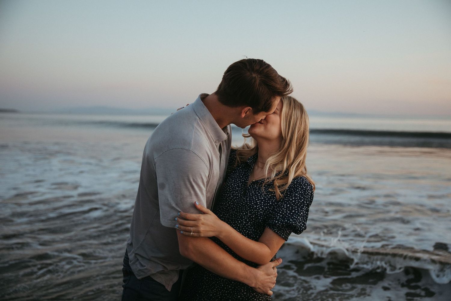 A couple shares a tender moment on the beach as the sun sets over the ocean.