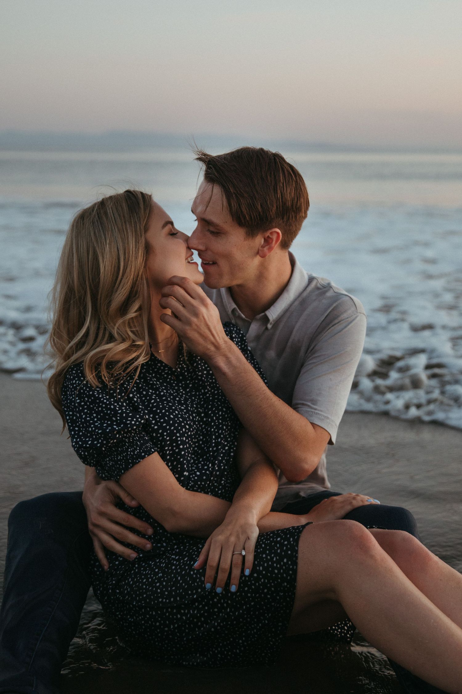A couple shares an intimate moment while sitting on wet sand at the beach.