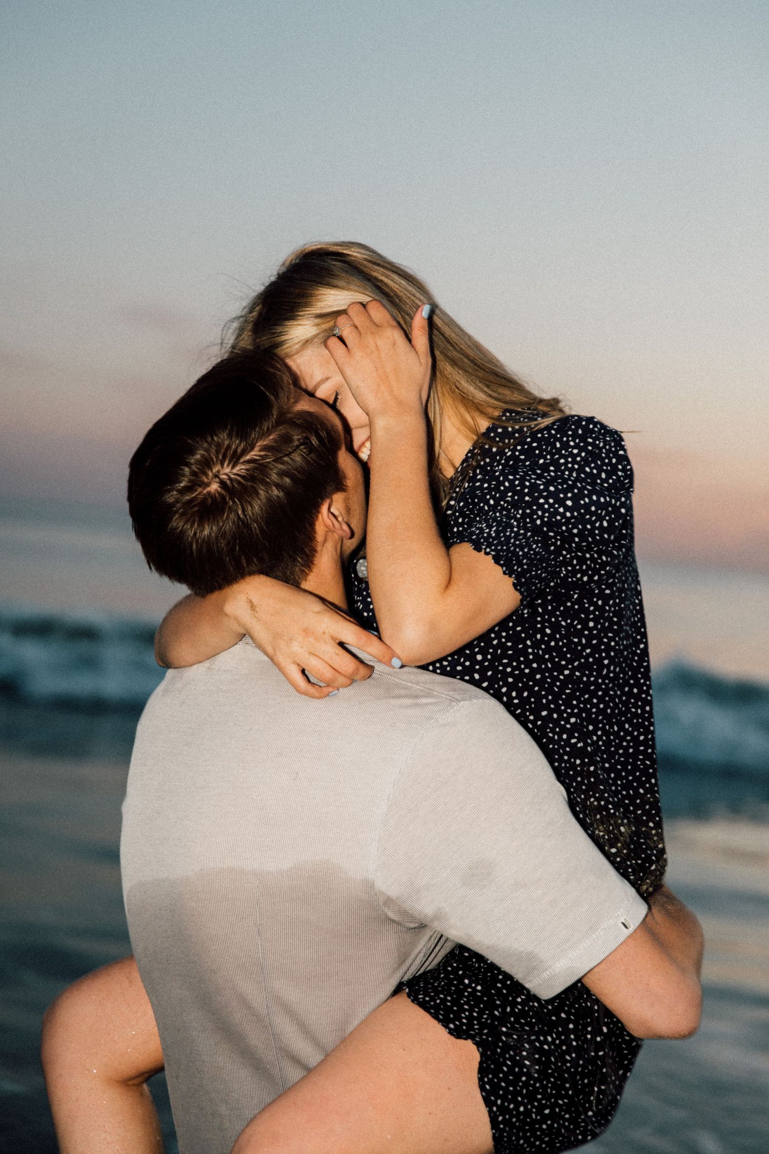 Passionate beach embrace with a couple in casual attire against the setting sun.