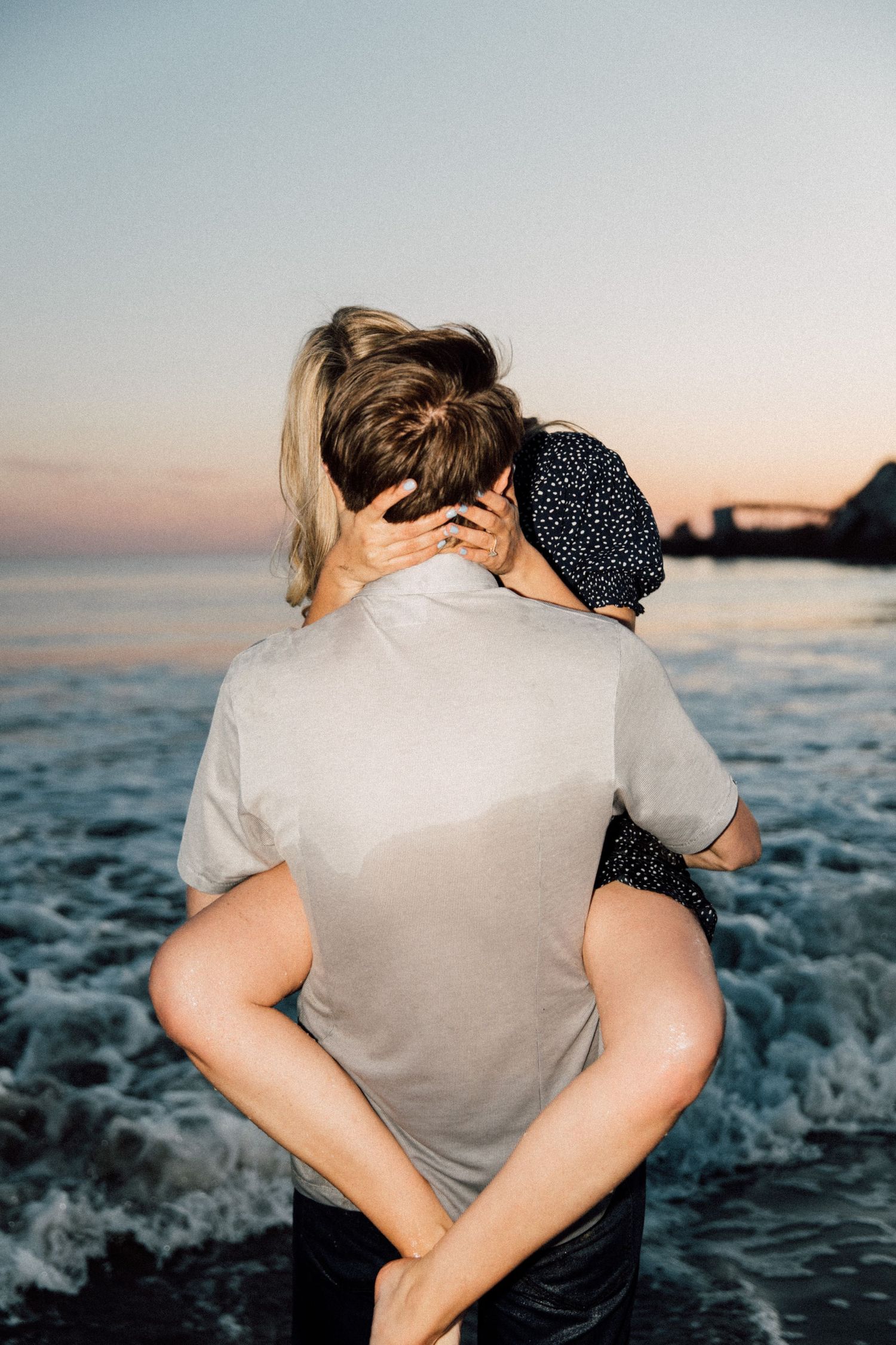 Silhouetted couple sharing an intimate moment on the beach with waves in the background.