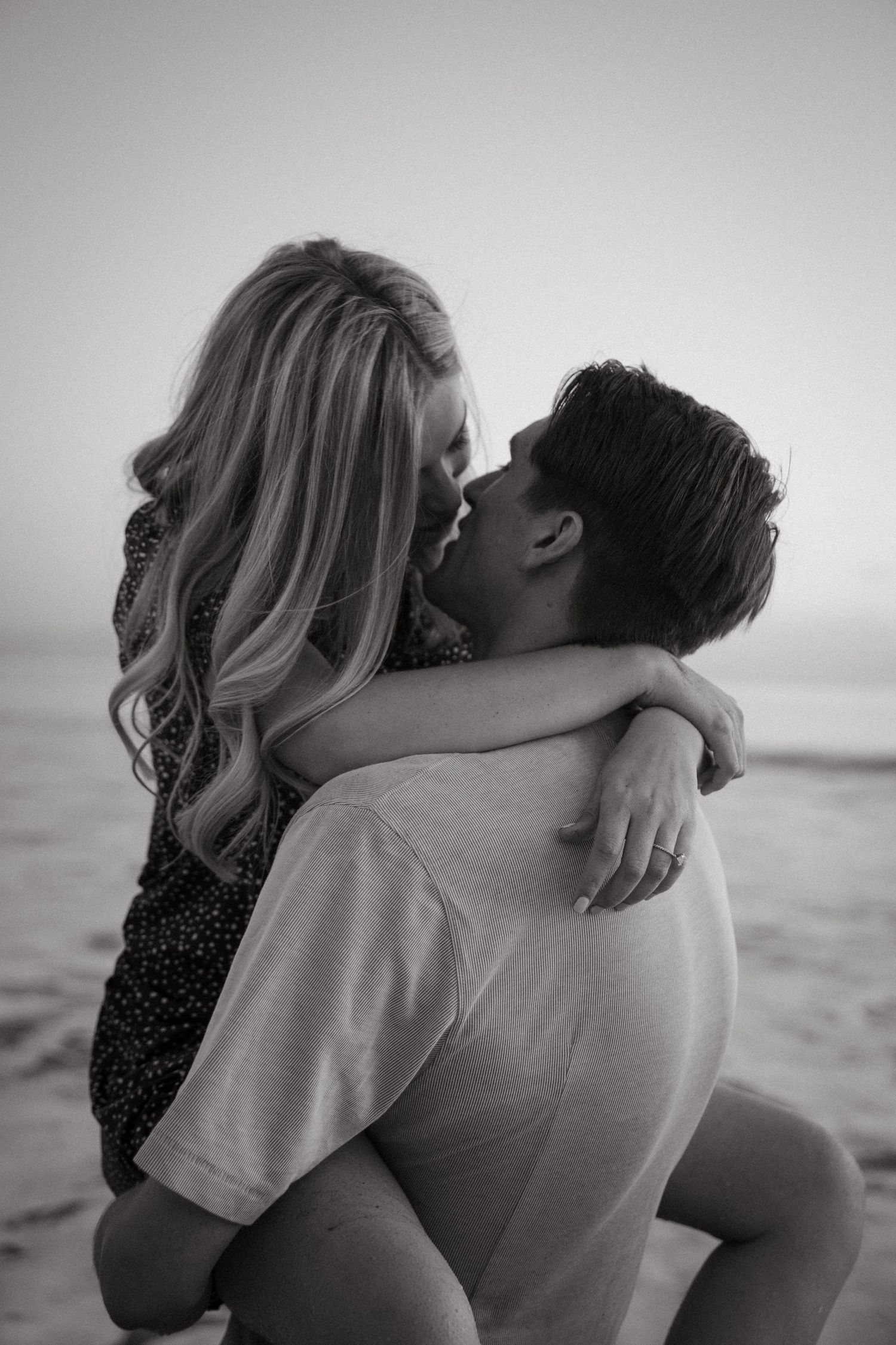 Black and white portrait of a couple sharing a tender moment on the beach.
