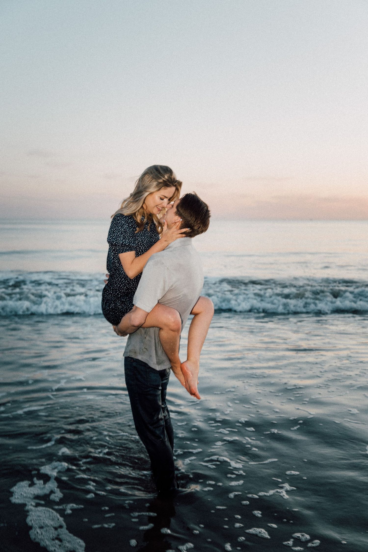Romantic couple playing in the ocean waves during sunset.