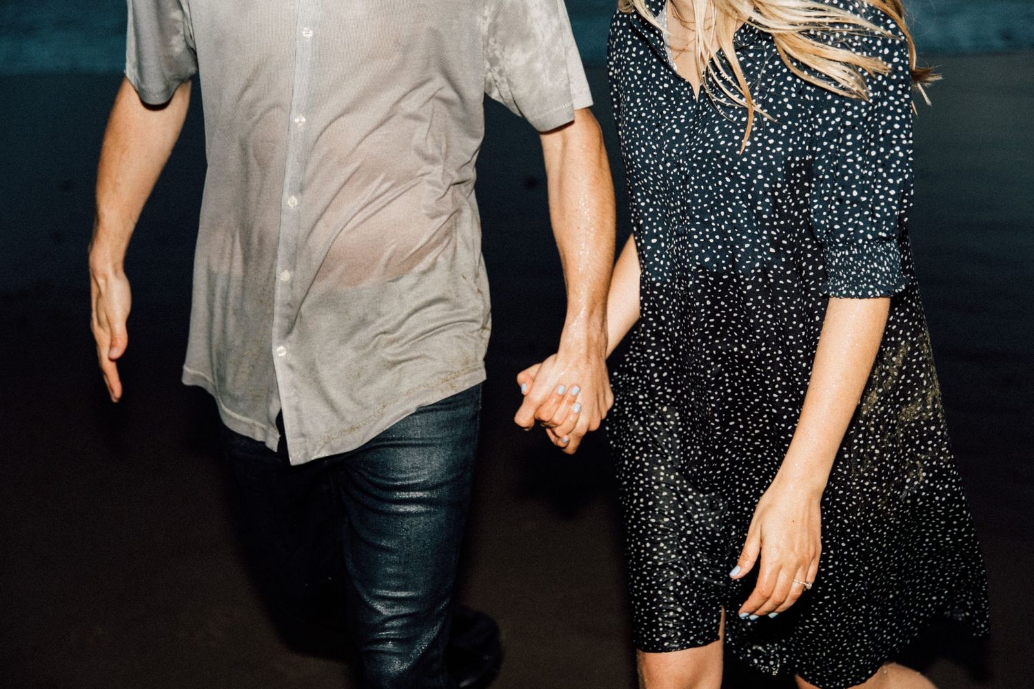 Couple walking hand in hand wearing casual attire near the ocean.