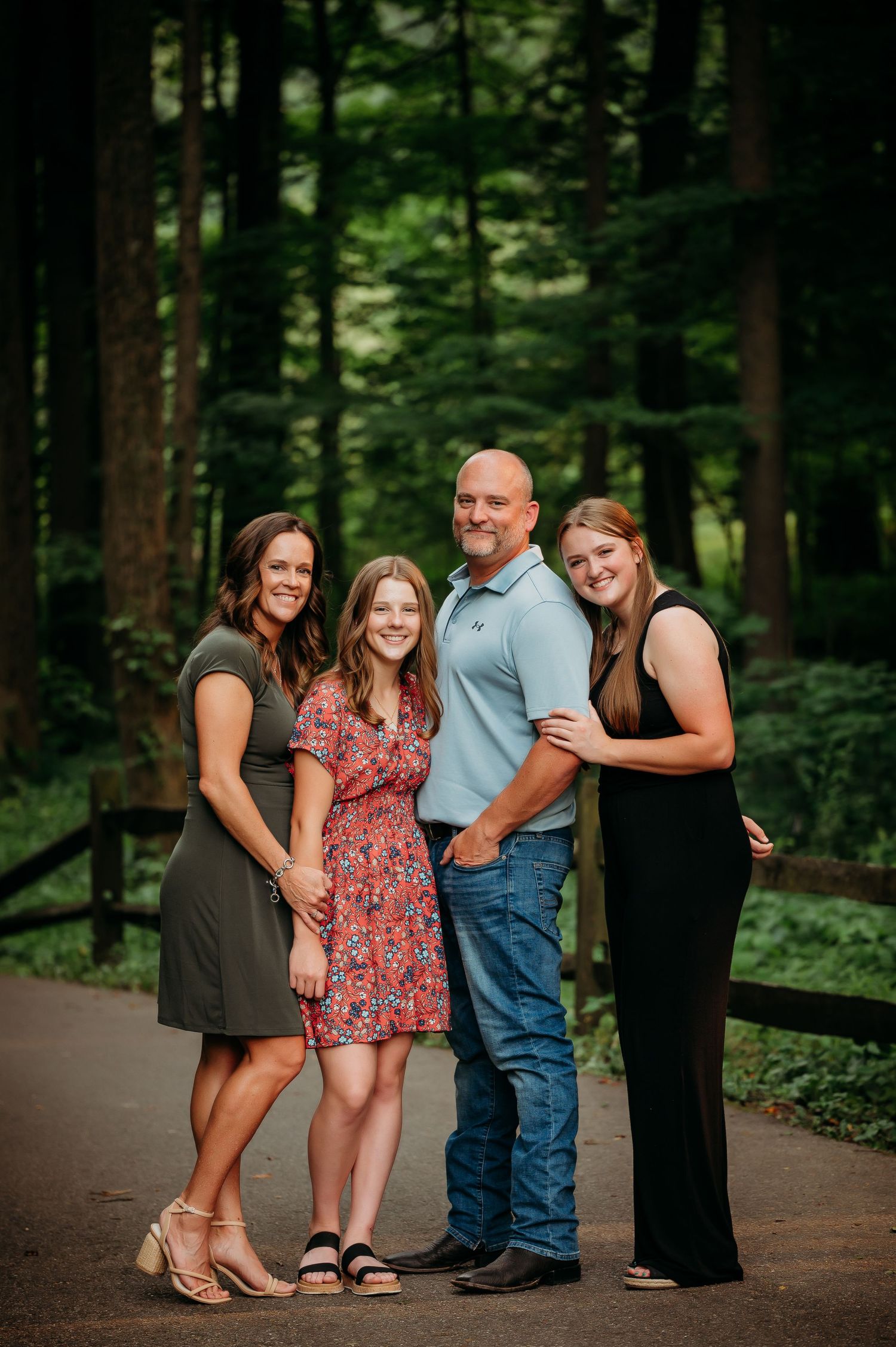 Family of four posing together on forest path during summer portrait session.