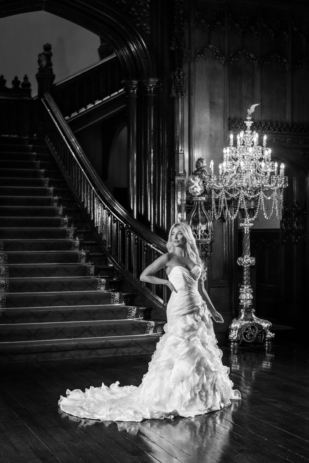 Black and /wite portrait of a bride in a dress at the bottom of a staircase in a stately home.