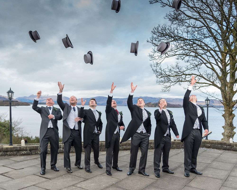 Groom and Groomsmen throwing top-hats in the air in front of a Scottish Loch