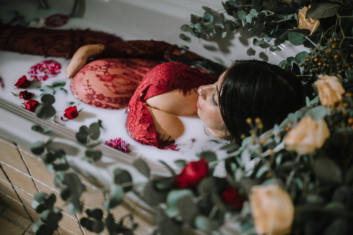 Milk bath with expecting mother in a lace red dress and florals inside and surrounding the tub in home in Vicenza, Italy.
