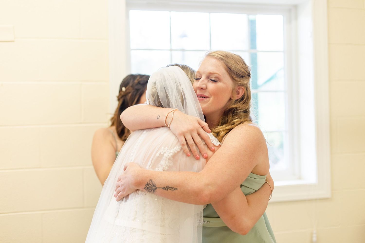 Emotional wedding party members embrace in a bright indoor space.