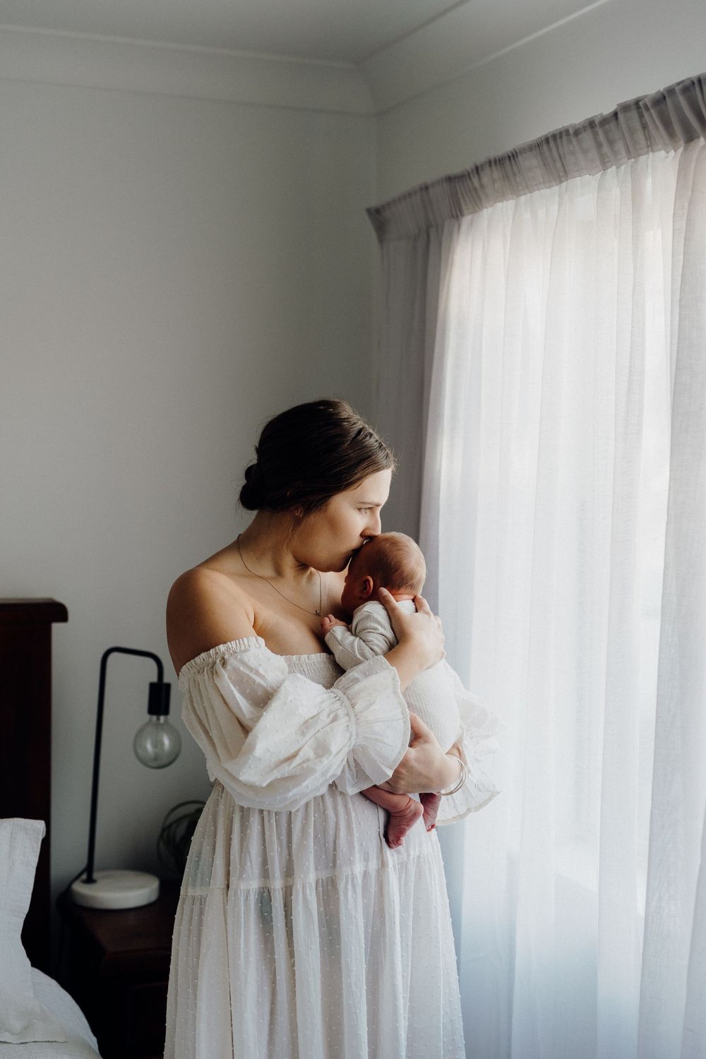 Tender moment by a window with white flowy dress in soft natural light.