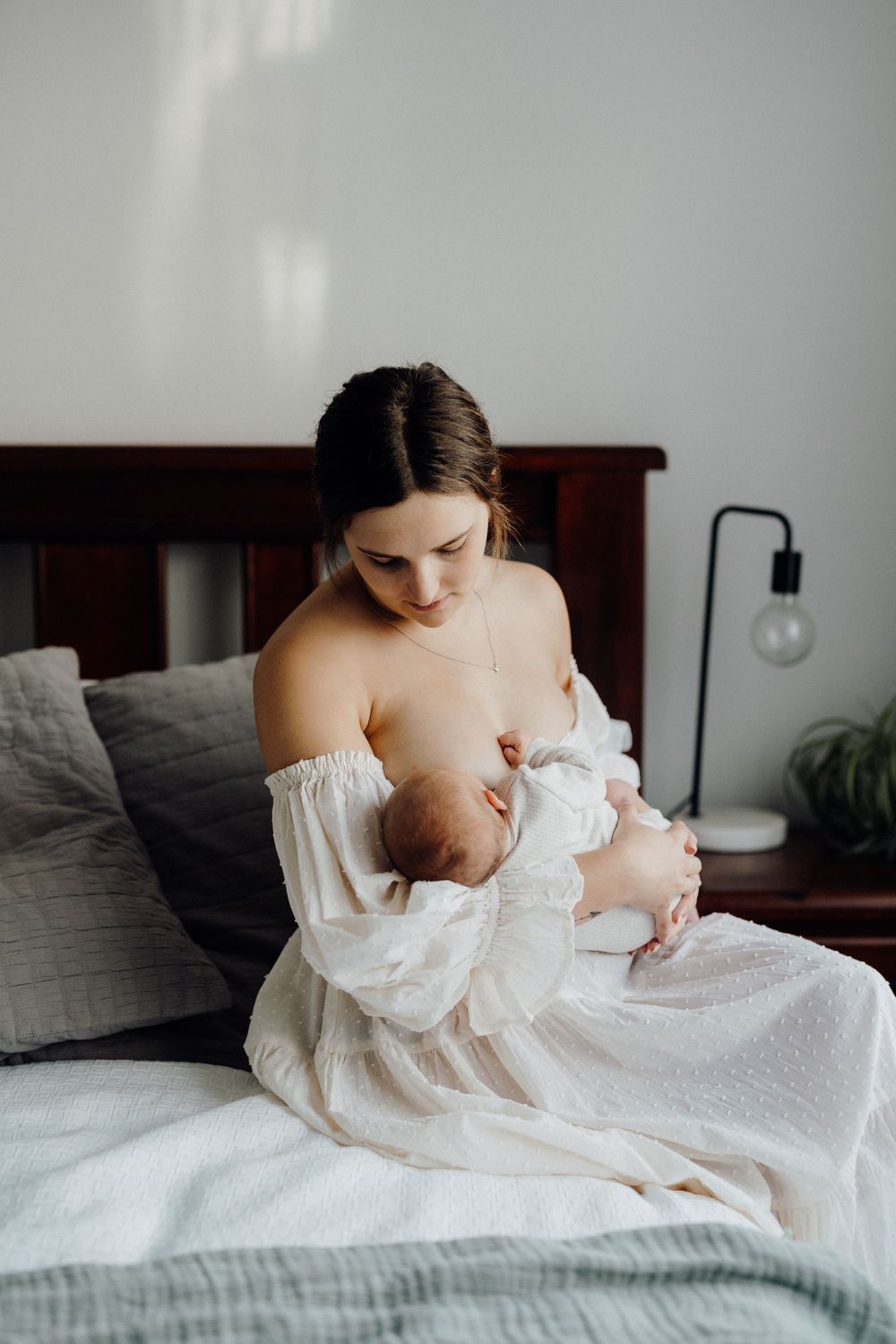 Intimate nurturing moment between caregiver and infant on bed beside window.
