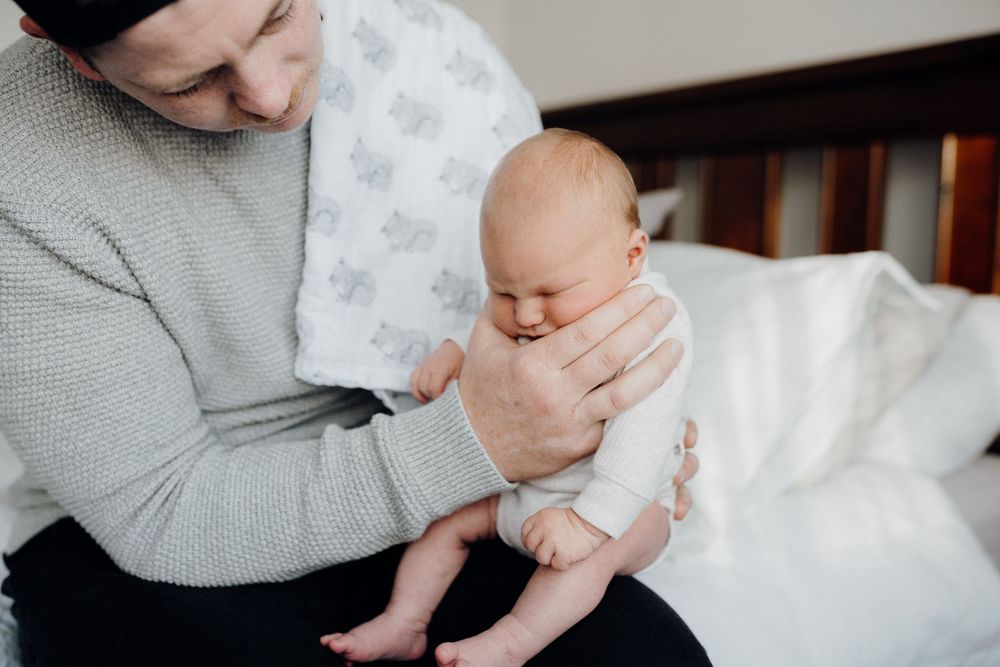 Tender moment as adult hands hold and comfort small baby on patterned bedding.