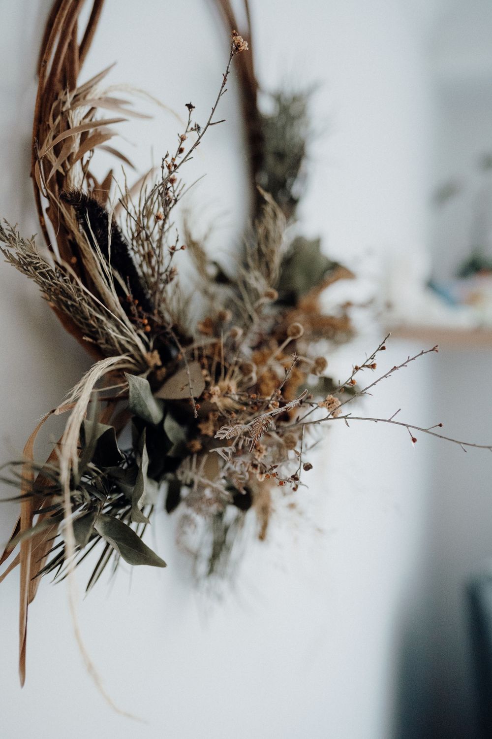 Artistic dried flower arrangement with brown tones mounted on white wall.