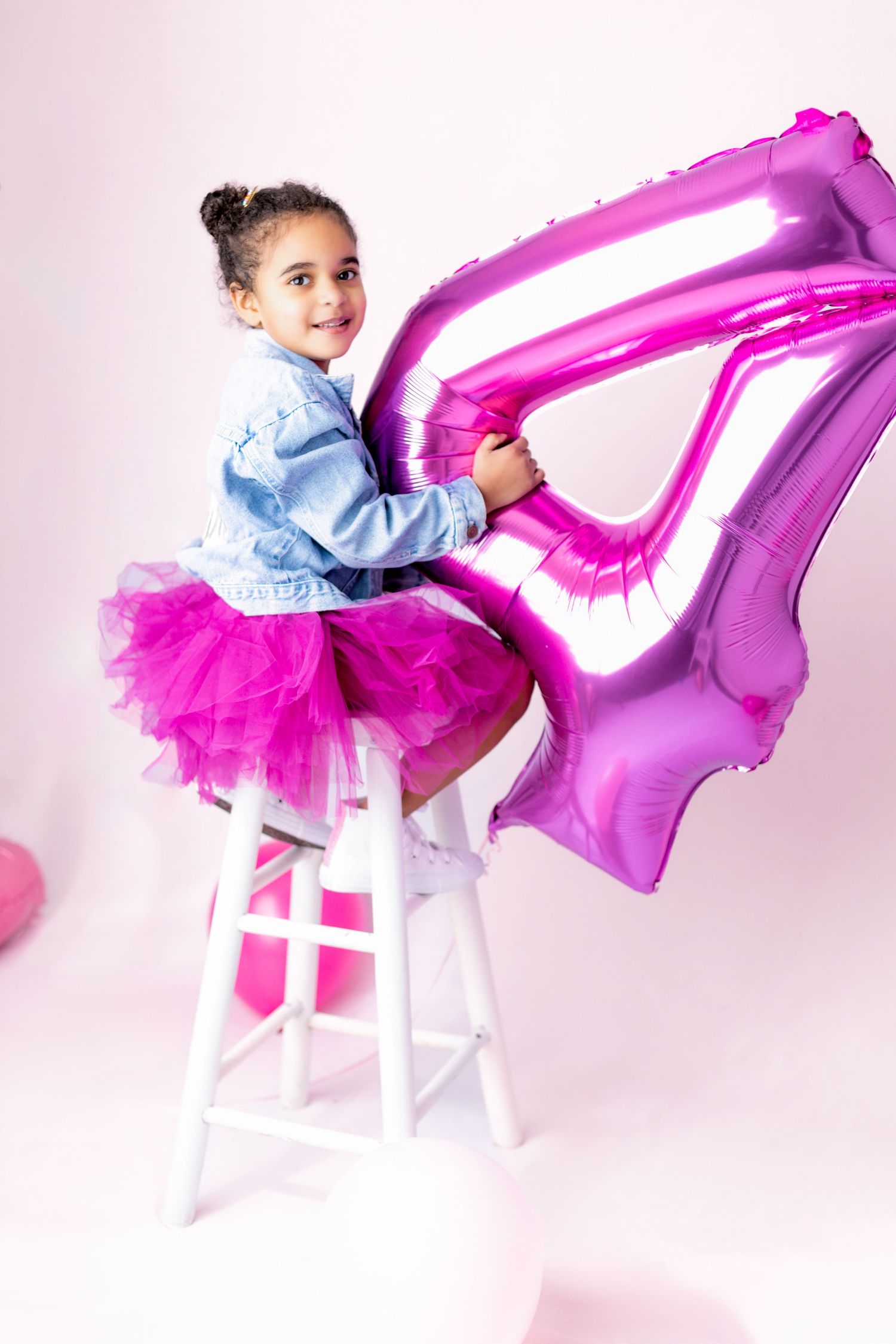Child in denim and pink tutu poses with metallic balloon on white background.