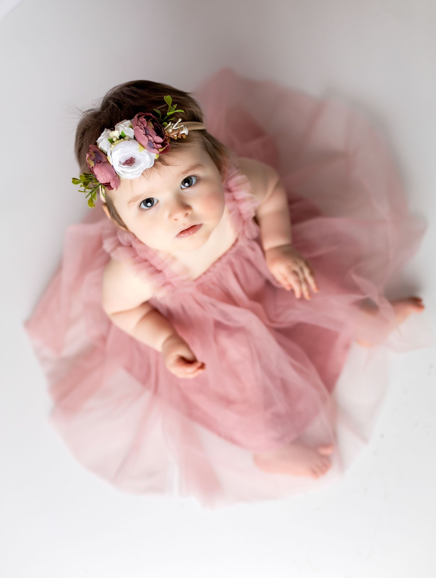 Overhead view of baby in pink tulle dress with floral headpiece.