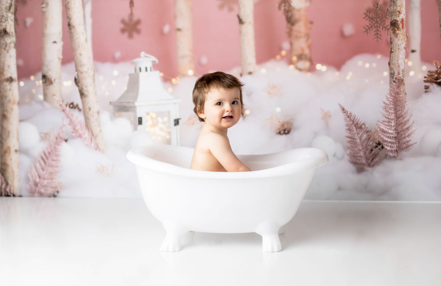 Child in bathtub prop with winter wonderland backdrop and pink tones.