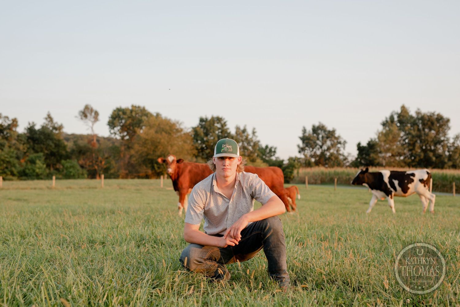 Pastoral scene with farmer crouching in green pasture as cattle graze in background.