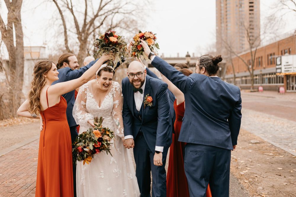 Bride and groom holding hands walking through floral arch created by wedding party with autumn bouquets outdoors.