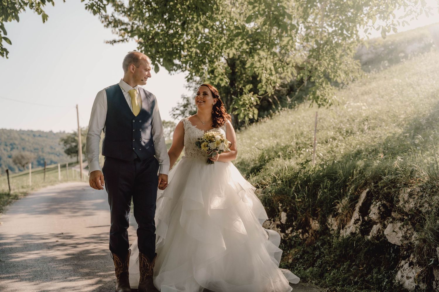 Sunlit outdoor wedding scene with couple walking through natural greenery.