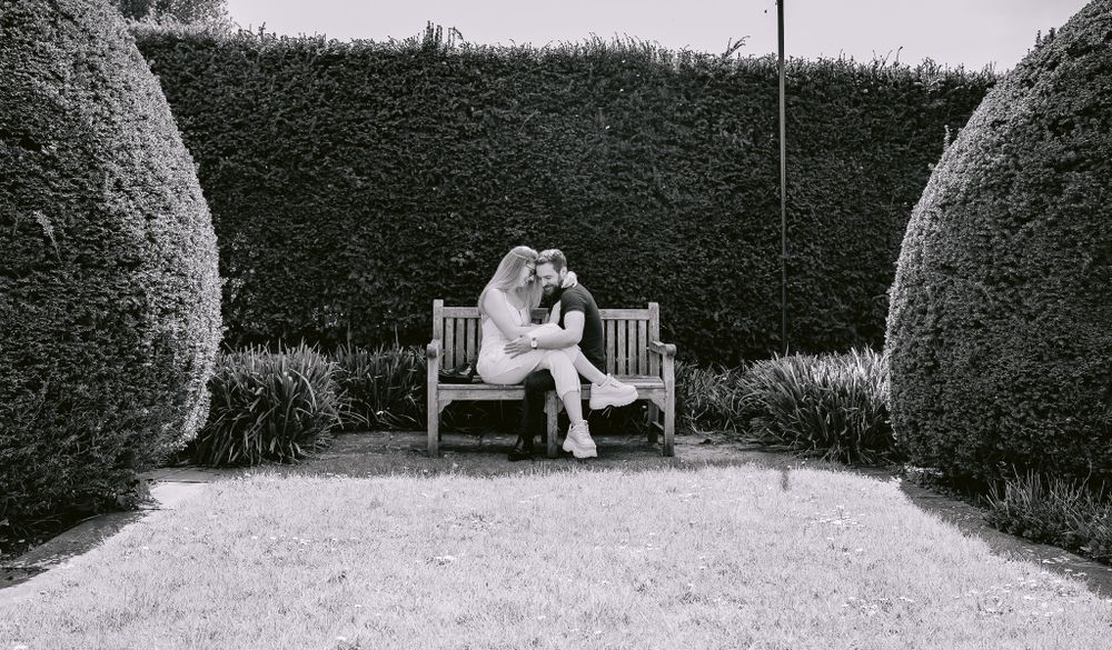 Black and white romantic portrait of couple sharing moment on garden bench.