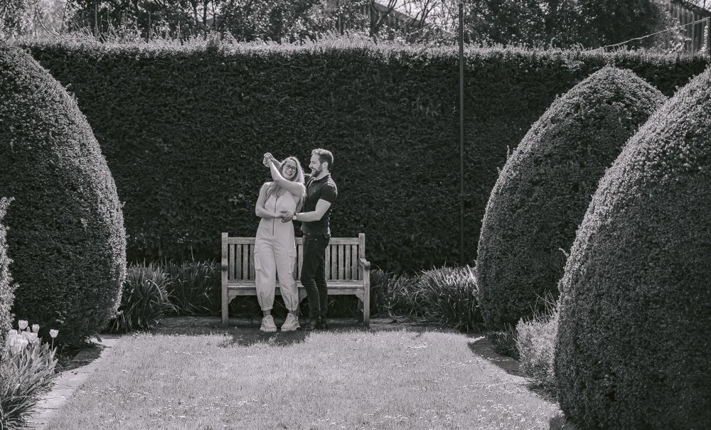 Black and white photo of couple on garden bench framed by manicured hedges.